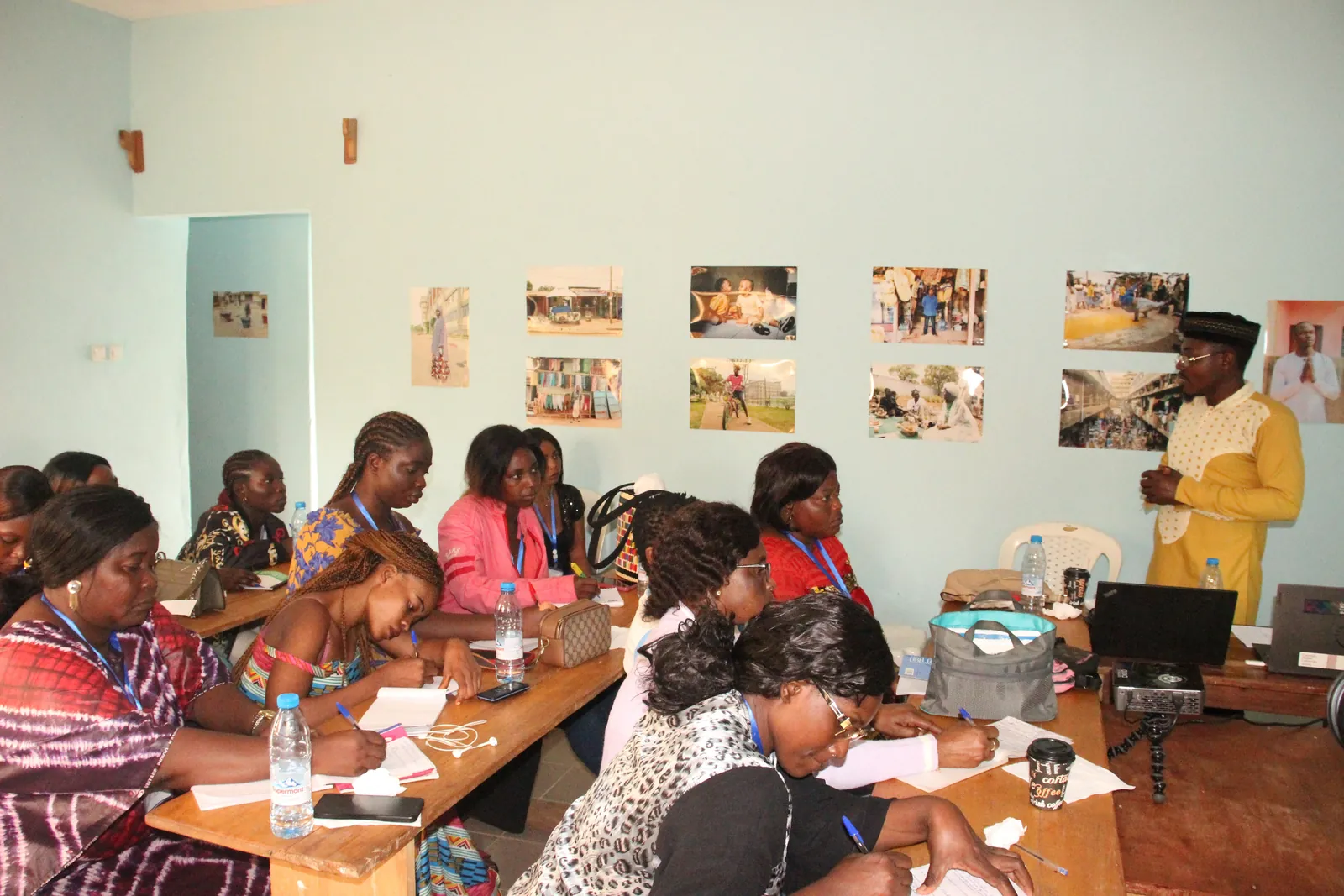 Participants writing at their tables during a training, photographs on the walls of the room