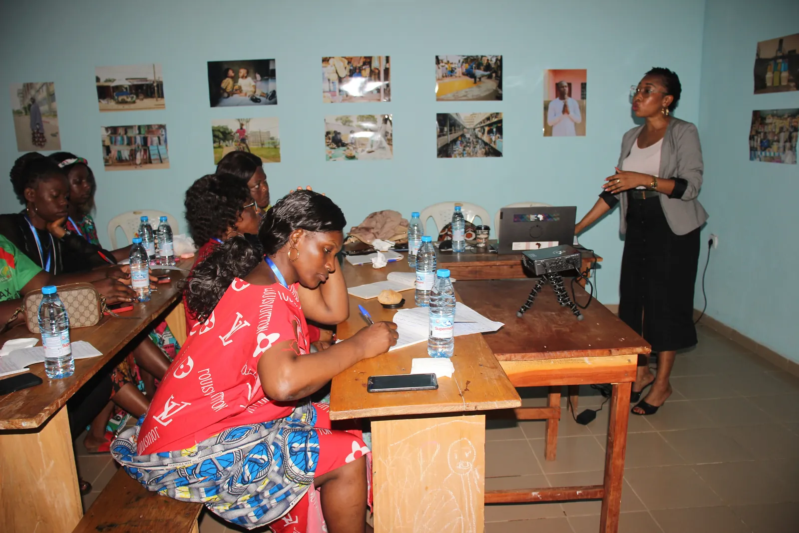 Refugee women taking notes during the Empower Her Through Innovation training, a facilitator standing by the projector
