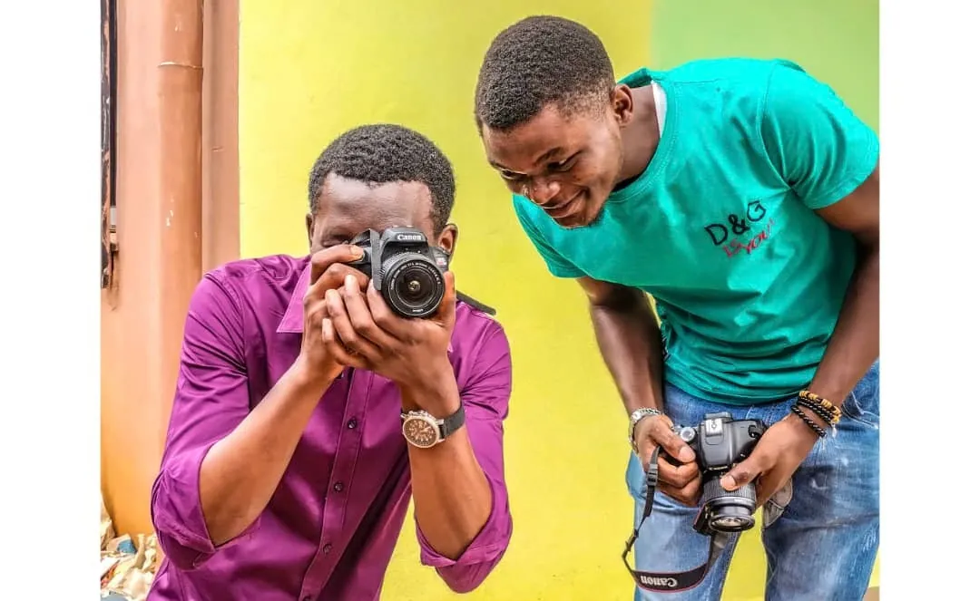 Two young men practising photography, one framing a shot while the other checks his camera