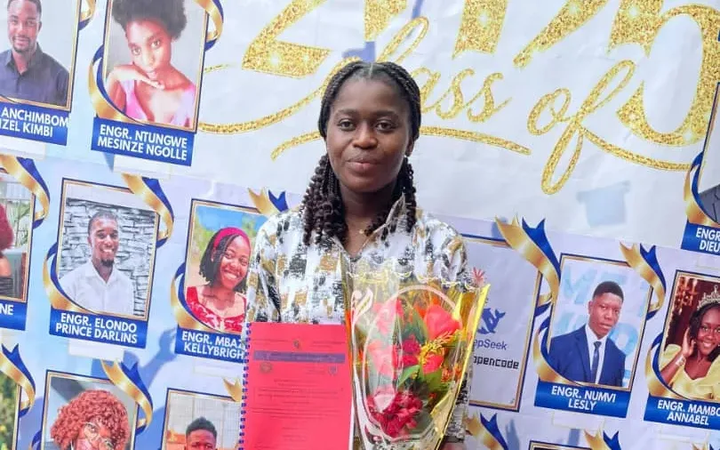 Fru Patience Ndeusse holding her degree and a bouquet of flowers in front of the banner of her graduating class